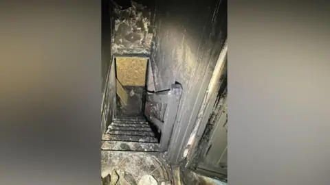 Jo Barnes A burnt stairway in a house viewed from the top, everything is burned black by the flames and smoke