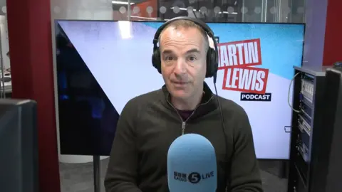 Martin has short dark hair and is wearing headphones and a green quarter-zip jumper.