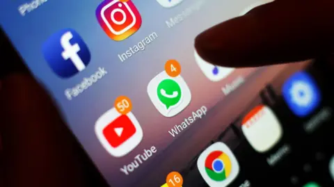 PA Media This is a close up photo of a screen. A finger is seen going to tap on a WhatsApp icon on a smart phone. There are several other apps on the screen, including YouTube, which has 50 notifications showing. 