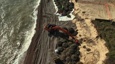 Shaun Whitmore/BBC An aerial image of part of the Thorpeness coastline. It shows where the sea meets the coastline and a digger putting piles of rock bags on the sand.