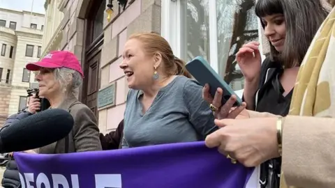 Three women who are part of a pro assisted dying group. They are seen celebrating outside the court building. 