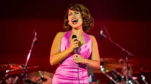 Getty Images A woman wearing a pink dress holding a microphone and singing. 