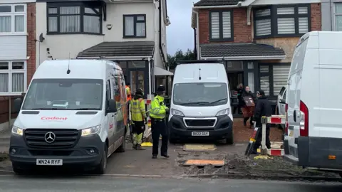 Police activity at a house in Broad Avenue. Officers are standing outside a house while a number of crime scene investigators can be seen leaving the house carrying items