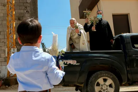 Karamallah Daher / Reuters A priest stands on the back of a truck as he visits neighbourhoods in Qlayaa, Lebanon, on 28 March 2021