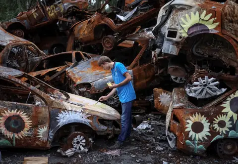 Gleb Garanich / Reuters Ukrainian artist Viacheslav Rybka paints a car destroyed during Russia's attack on the town of Irpin on 10 August 2022
