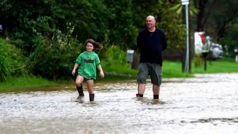 AFP Two people walk along a flooded road in New Zealand