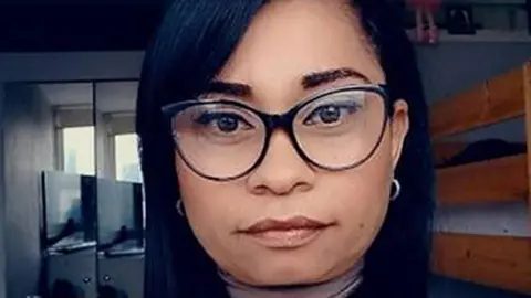 A woman with dark straight hair, black framed glasses and silver earrings 
