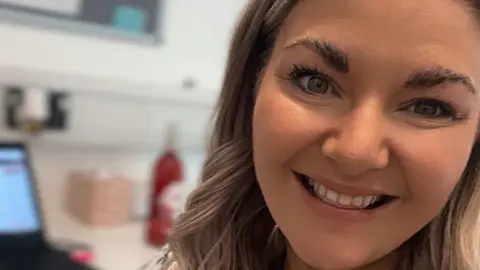 Siobhan Gorman A selfie of Siobhan Gorman who has long wavy blonde hair and is smiling. She is in an office.