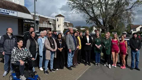 A large group of people standing outside some shops. 