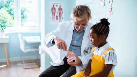 Marko Geber A dentist teaching a child how to brush their teeth.