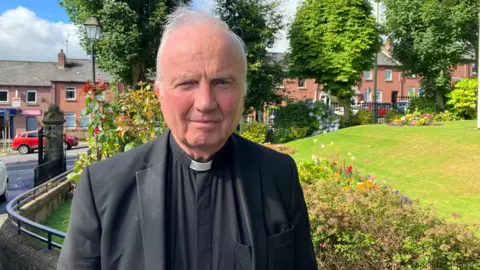 Bishop of Derry Donal mckeown stands in front of flowers in Brooke Park