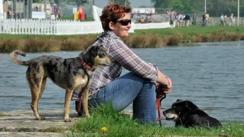 Badminton Horse Trials A woman sits with her two dogs at the lake in Badminton's cross country course.
