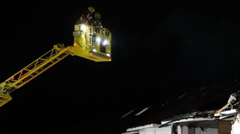 PA Media A cherry-picker with fire crew in it looms above an exploded roof