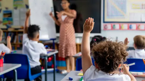 A generic view of students in a classroom, with three pupils raising their hands.