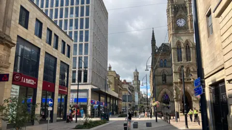 A moderately busy city centre street. On the left is a Pret a Manger on the right is the famous Bradford Waterstone's building