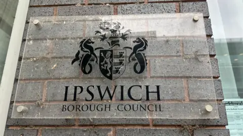 Alice Cunningham/BBC A sign on a grey brick building that reads Ipswich Borough Council with its logo on it. 