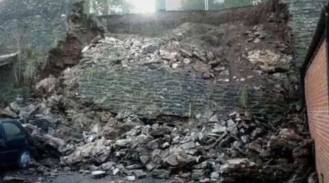 BBC A collapsed grey stone wall with blocks of stone, including one large section extending to the ground below.