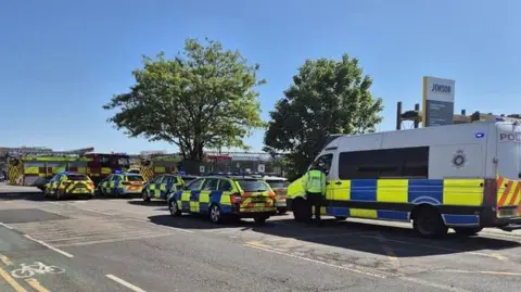 Parked police vans, cars and fire engines parked near a Jewson in Northampton. 