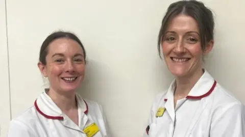 Alex Davis (left) and Rachel Evans are both wearing a white nurse's uniform. They both have brown hair which is tied back.
