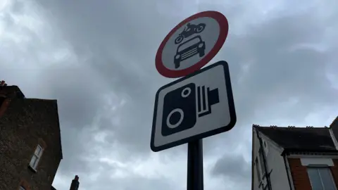 Circular red sign with car and bike inside and square camera sign just below