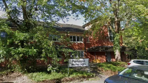 Google A two-storey brick building surrounded by several trees, with cars parked in front and a sign saying Pontypool Medical Centre.