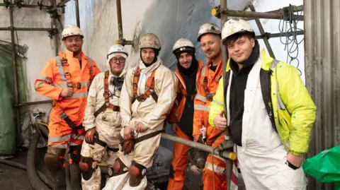 LDRS Six men in PPE looking towards the camera as they stand on the scaffolding on the bridge.