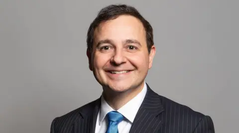 UK Parliament MP in shirt, tie and suit smiling for the camera