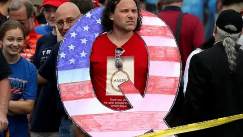 a man poses with a Q sign at a Trump rally