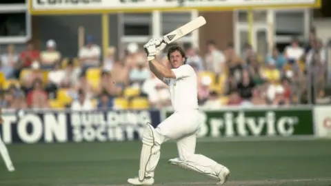 Sir Ian Botham on the field with a cricket bat