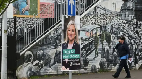 Getty Images Sinn Féin's Michelle O'Neill election poster is seen against the backdrop of a republican mural in the nationalist area of west Belfast