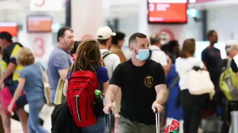 Getty Images Traveller arriving from Melbourne wears a mask as he wheels baggage through crowd at Sydney domestic airport on 2 July 2020