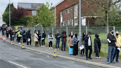 PA Media People queue for the vaccination centre at the Essa Academy in Bolton.