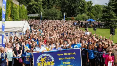 Stars Appeal A large crowd of people taking part in the Stars Appeal walk. They are all gathered, looking at the camera and cheering. The people at the front are holding a Stars Appeal banner.