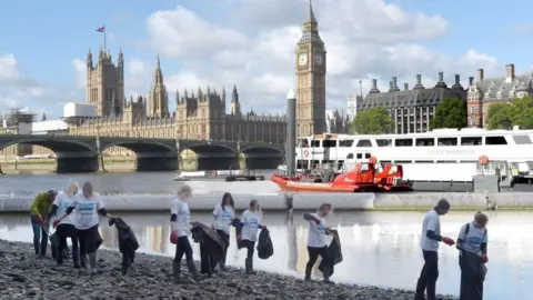 London Aquarium staff clean up bank of South Bank with Parliament behind them