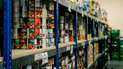 Shelves of canned food, including chopped tomatoes at a food hub. 