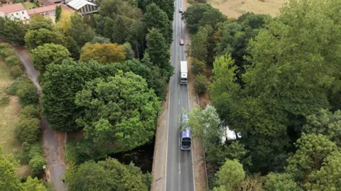 Aerial image shows a bus, lorry and two cars crossing a single-carriageway road bridge.