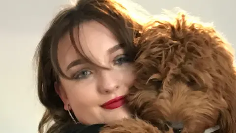 Family photo Amber Walker is pictured in a warm embrace with a light brown dog. She has dark hair, silver hoop earrings and make-up including dark red lipstick.