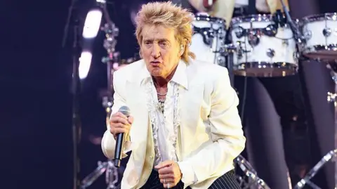 Getty Images Sir Rod Stewart pouts on stage while holding a microphone.