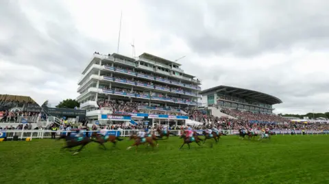A general view as runners pass the winning post during The Aston Martin 'Dash' Handicap on Derby Day during the Derby Festival at Epsom Downs Racecourse on June 01, 2024 in Epsom, England.