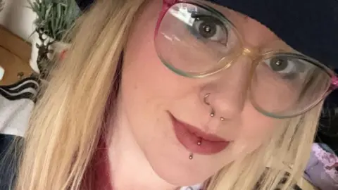 Tamara Beattie Tamara Beattie. Tamara is a young woman with long blonde hair worn loose under a navy bucket hat. She has her nose and lip pierced and wears rainbow coloured glasses.