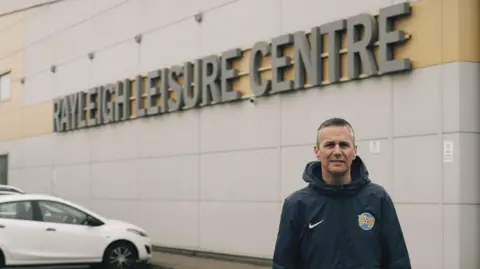 Richard Southwood from Football Fun Factory stands in front of Rayleigh Leisure Centre in a football tracksuit.