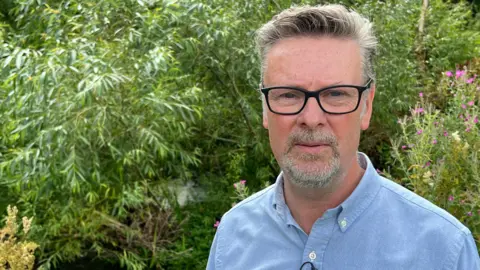 BBC Cotswold councillor Tristan Wilkinson stood in front of trees 