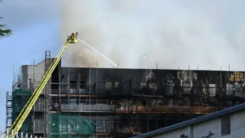 Getty Images Firefighters tackle a fire on a tower block from a crane on August 26, 2024 in Dagenham, England.