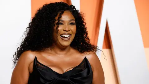 Reuters Lizzo smiling on the red carpet at the Vanity Fair party after the Oscars, in a sculpted black dress