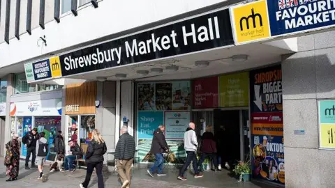 Getty Images People are walking into Shrewsbury Market Hall, which has a large black and white sign over the entrance, and another sign saying Britain's favourite market. There are adverts around the entrance and there is a coffee shop next door.