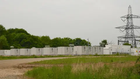 Images of a BESS site in Ipswich. The site looks like rows of metal containers and is based close to an electricity substation. 