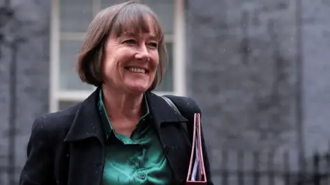 Reuters Jo Stevens in Downing Street. She is smiling, looking to the side of the camera and is holding a file under her arm. 