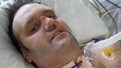 Cancer Research UK A man lying in a hospital bed with wires and monitors all over his chest and nose.
