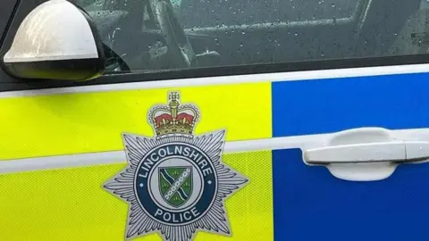 The door of a Lincolnshire Police car with blue and yellow blocks and the force's badge on the side