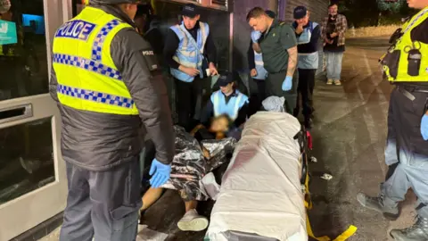 BBC A group of people helping a girl who is on the floor unconscious.